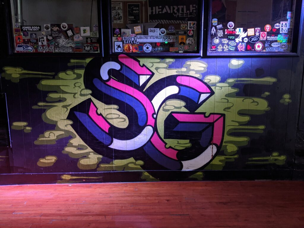 A colorful wall with "SG" painted on it, standing for Southgate Roller Rink. There are stickers all over the walls.
