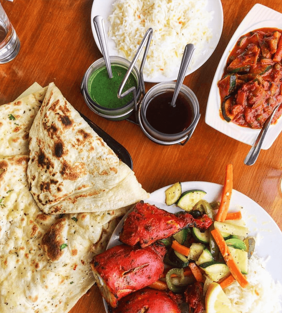 Table spread of tandoori chicken, naan, chutney, basmati rice, and curry dishes from Cedars Restaurant
