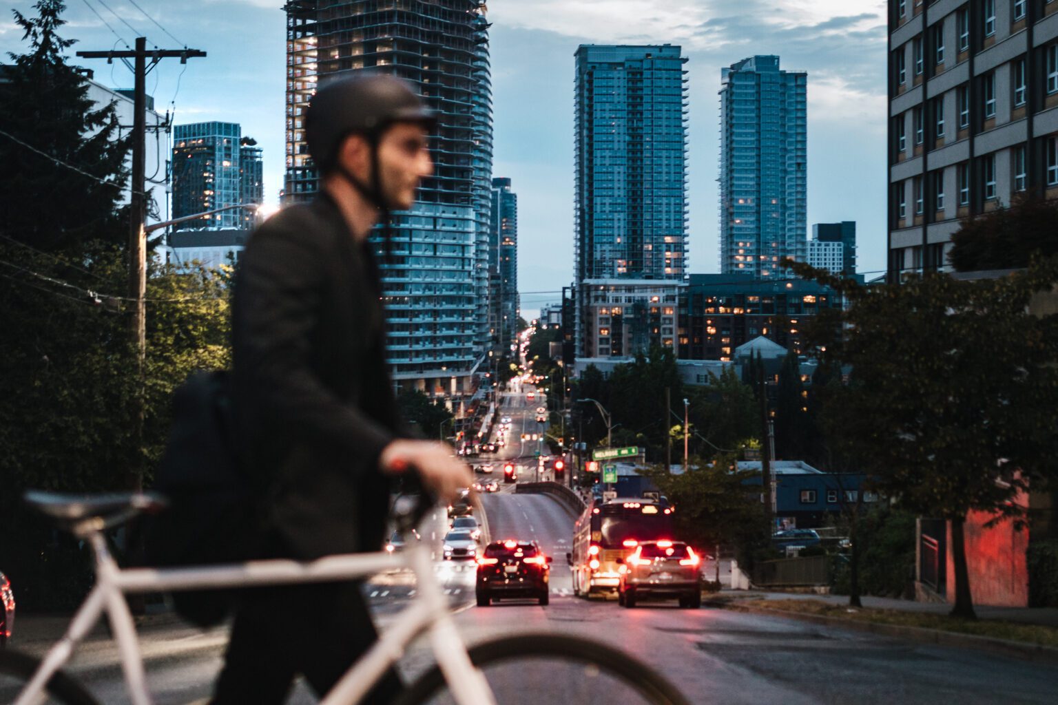 A business man wearing a blazer rides his bicycle through the city streets of Seattle, Washington, USA. He carries work items in a messenger bag slung over his shoulder. An environmentally friendly and healthy way to commute to work: sustainable lifestyle.