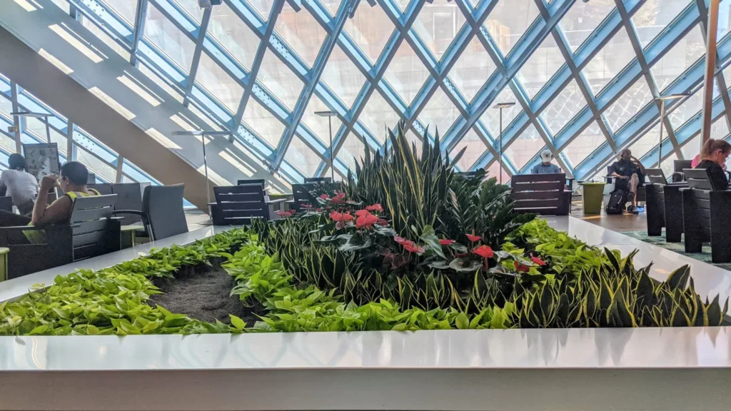A big living room inside the Seattle Central Library. There are many green plants in the center, in addition to seating around and computers.