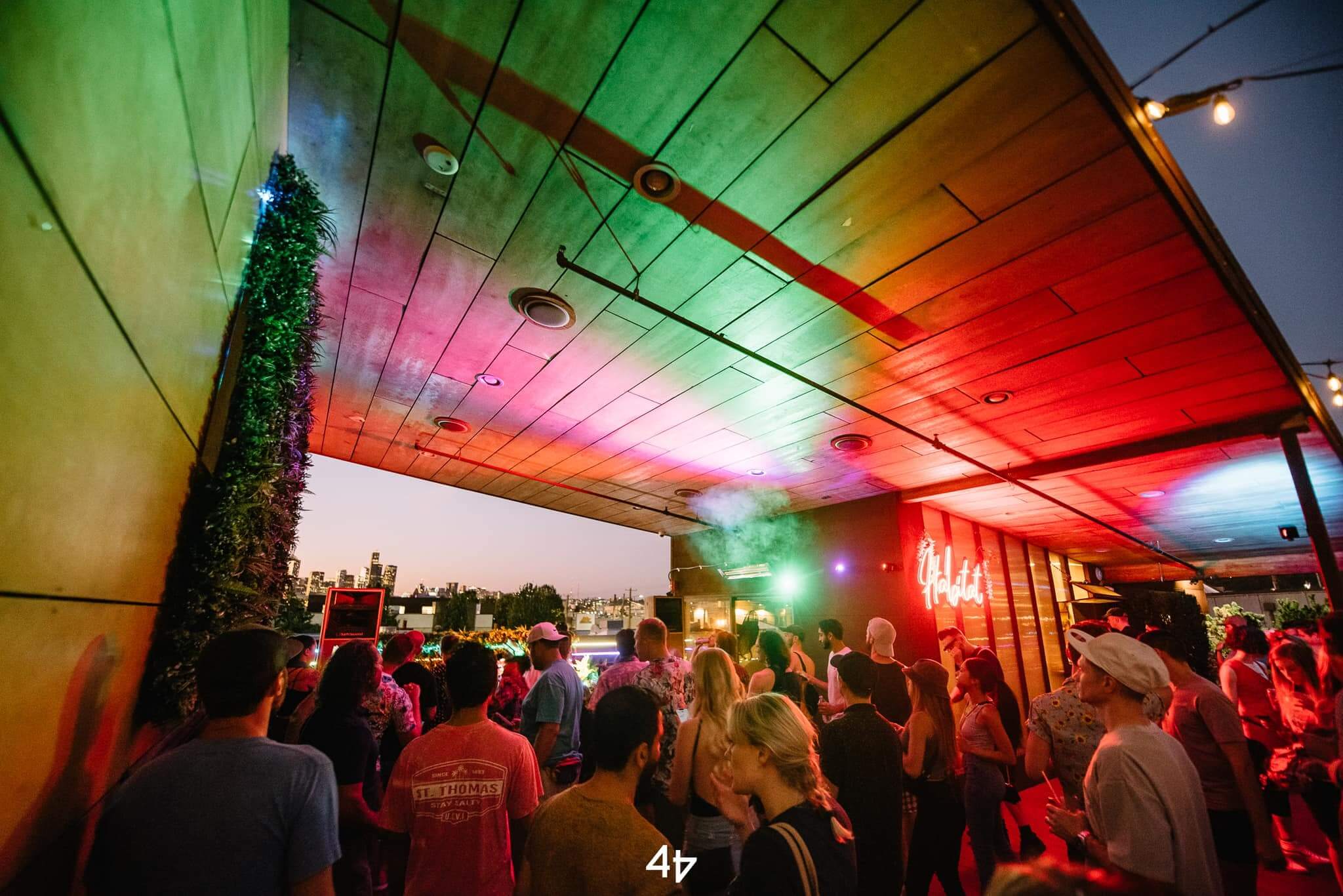 A colorful rooftop with vibey lighting where people are dancing to the sunset