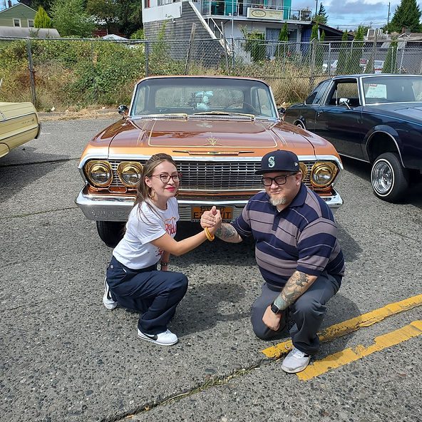 Two people kneel near a brown lowrider