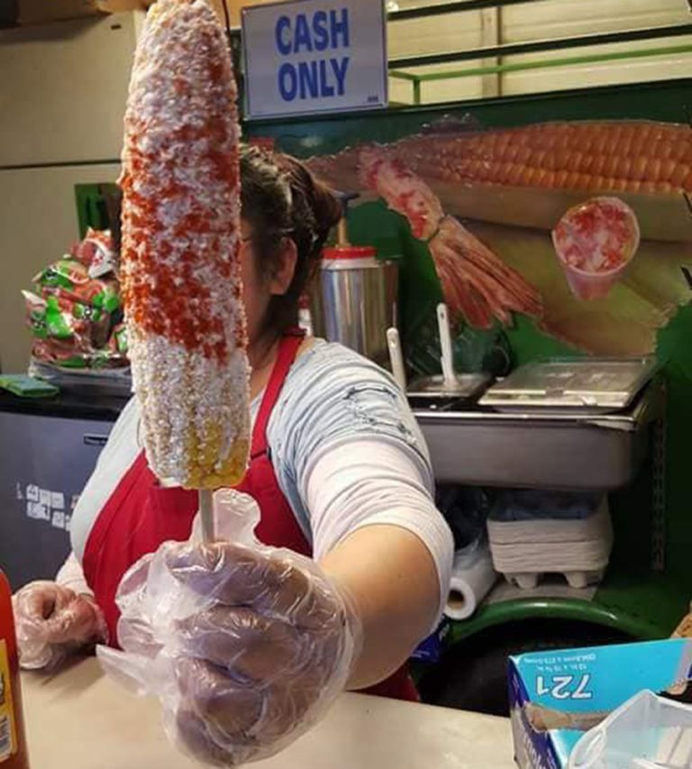 Worker giving a large ear of roasted corn, obscuring her face
