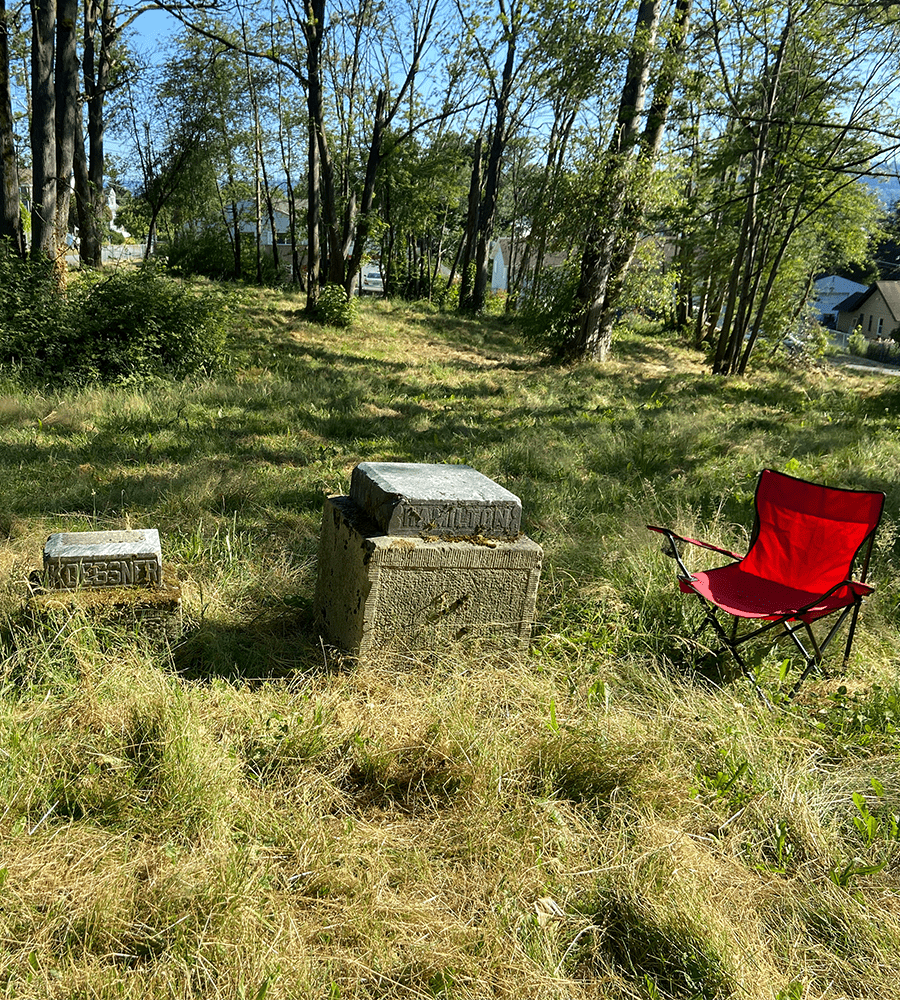A red folding chair sits next to unmarked graves in the daylight