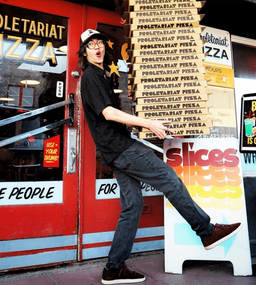 Proletariat Pizza employee striking a pose while balancing a towering stack of pizza boxes