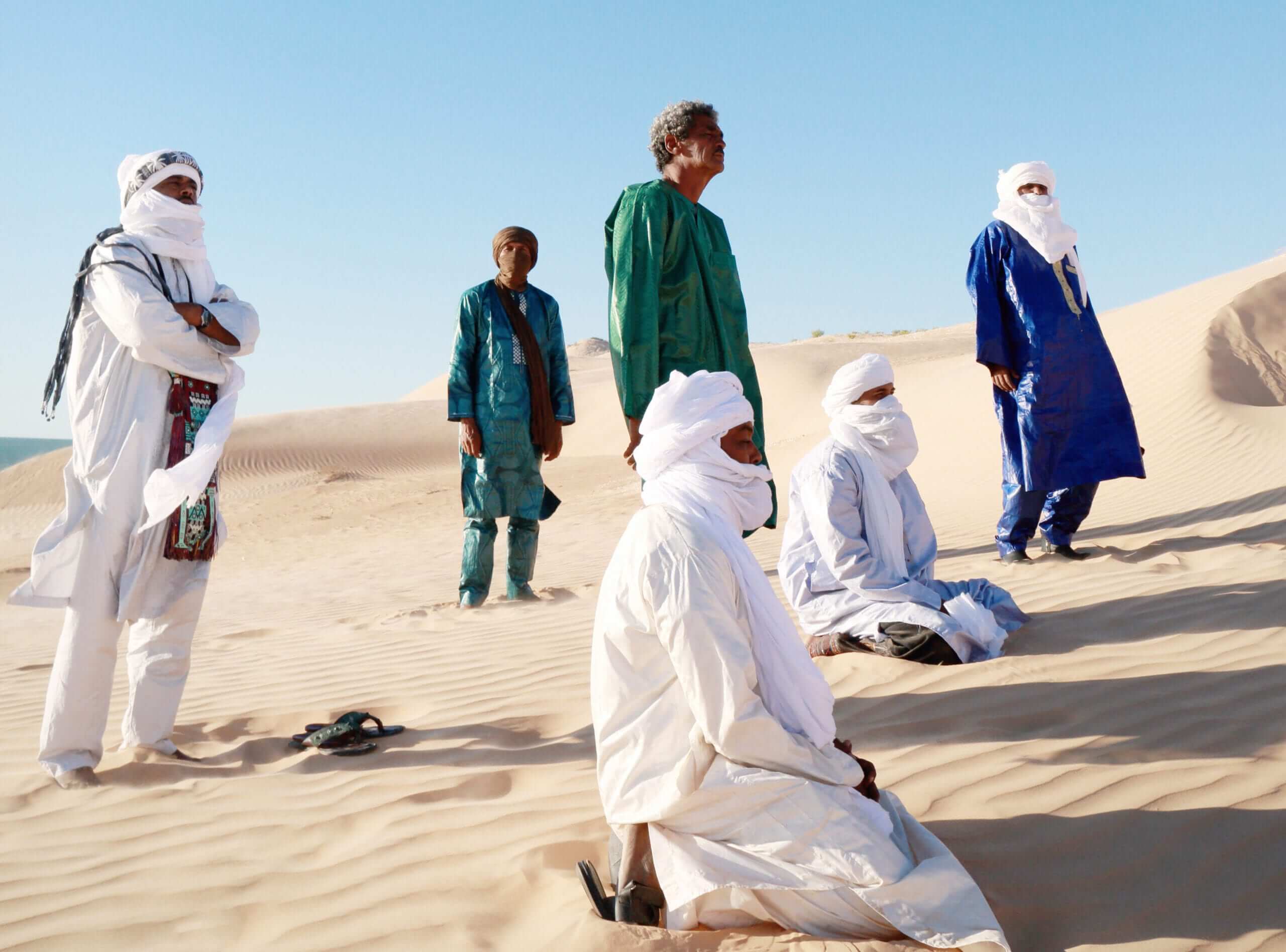 A band image: Tinariwen band members stand looking longingly at a desert vista