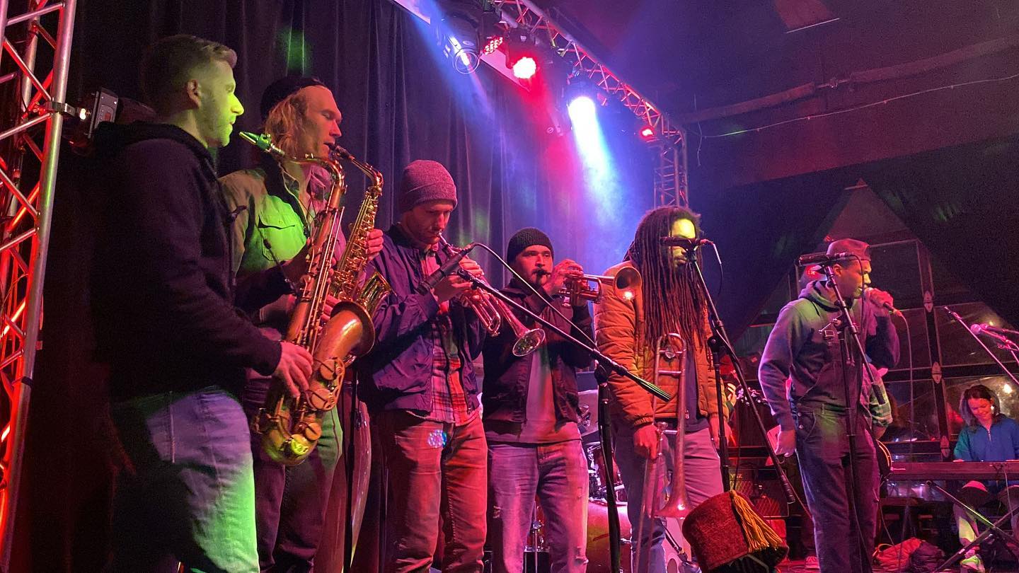 A group of musicians stand side-by-side playing onstage at Mo'Jam Mondys