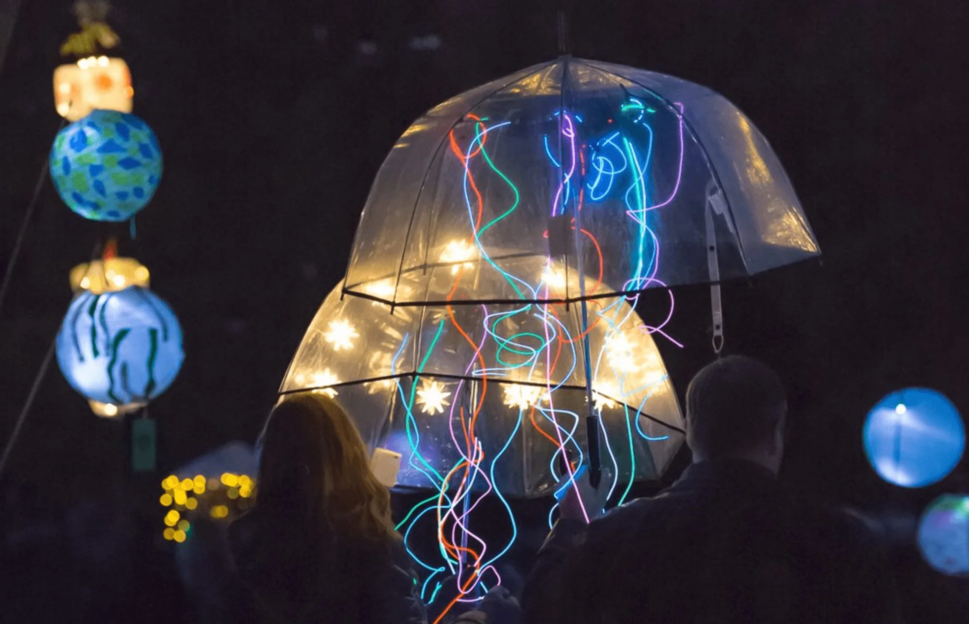 A colorful lightshow at the annual Luminata, featuring people holding umbrellas with bright string lights