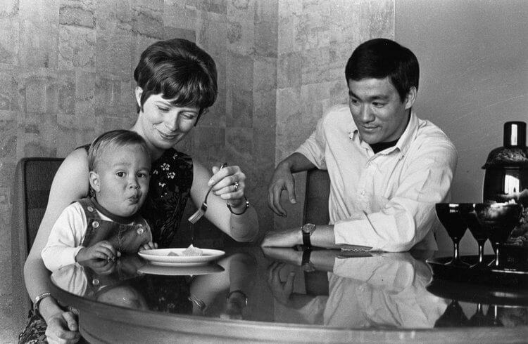 A photo of Bruce Lee next to his family. There's a baby eating.