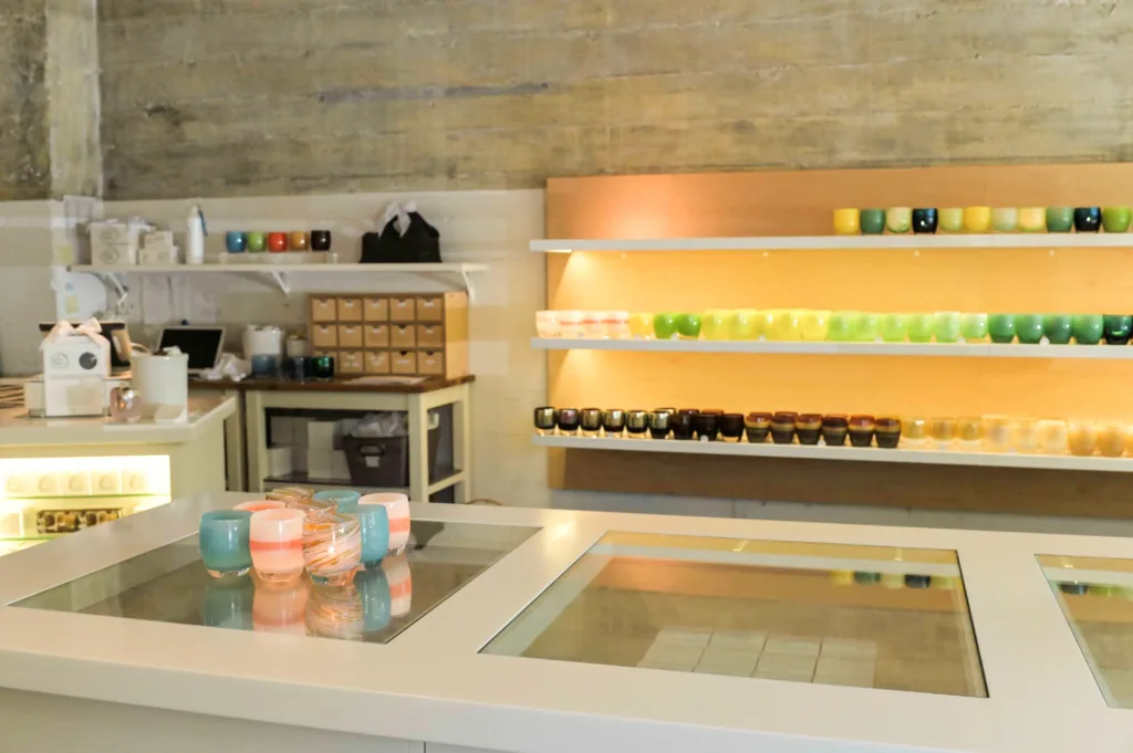 glassybaby candle holders sit on counter and on a shelf in the back of the glassybaby store