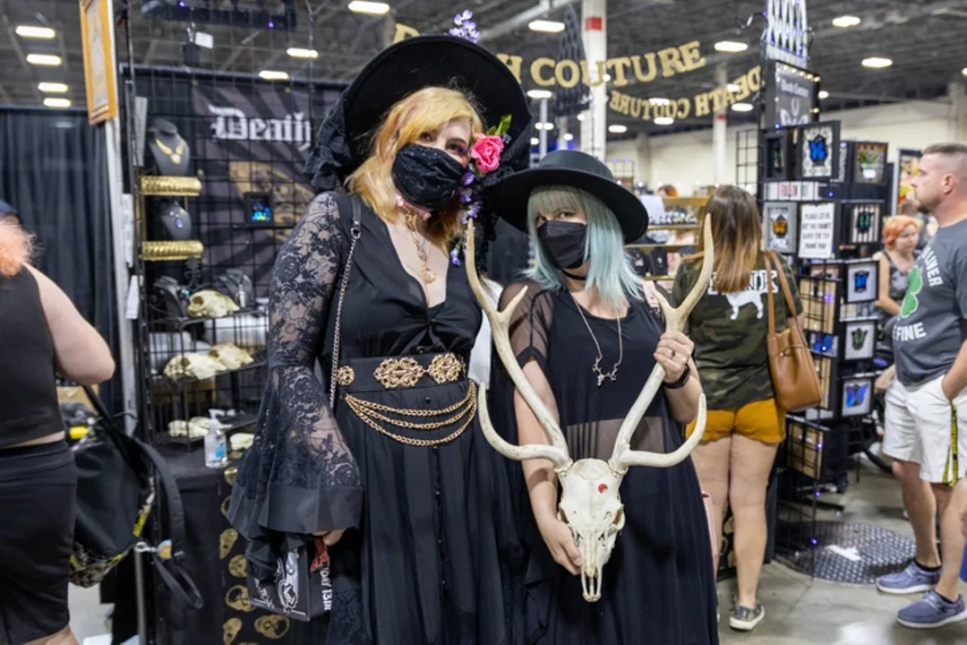 Two people in witches hats—one holding an antlered deer skull—pose for a picture at the Oddities and Curiosities Expo