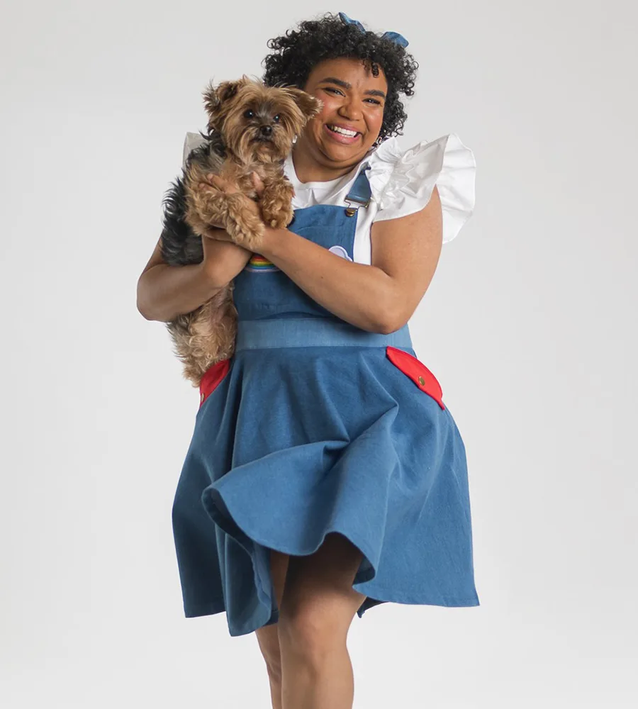 Kataka "Kat" Corn (they/them) stars as Dorothy, holding a little dog Toto