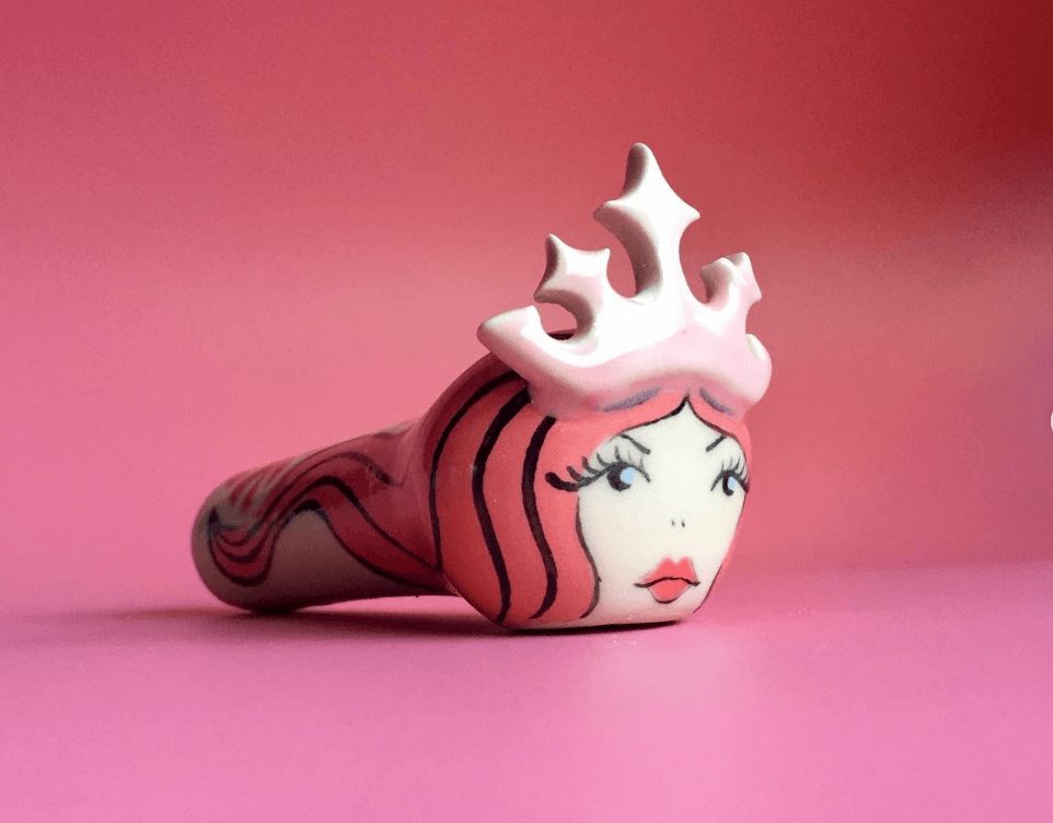 A "girl boss" Wonder Pipe, where the head of the bowl looks like a queen. The colors are mostly pink and white.