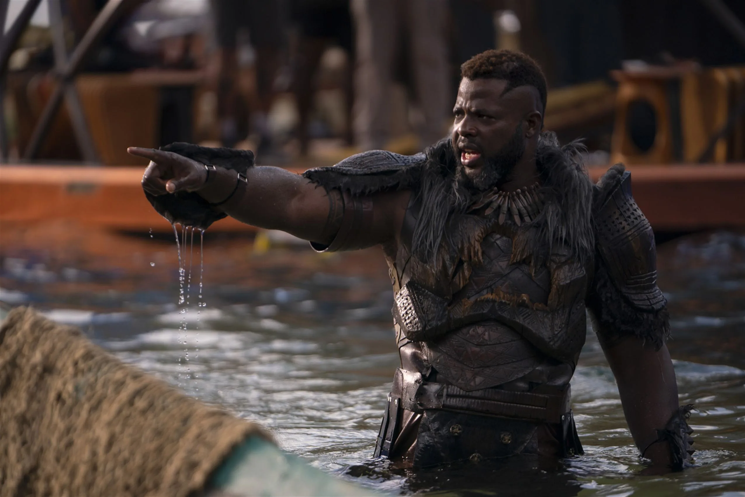M'Baku (played by Winston Duke) points offscreen while waist-deep in water