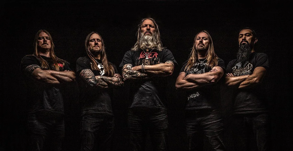 The band Amon Amarth poses with arms crossed against a black background