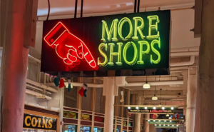 The "More Shops" sign at Pike Place with a finger pointing down to lower levels.