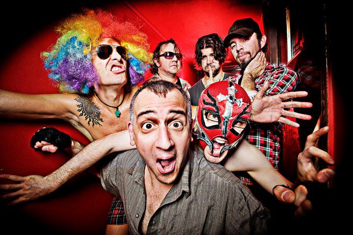 The Dwarves band poses all wacky together against a red background. One guy wears a luchador mask and one has rainbow hair with sunglasses.