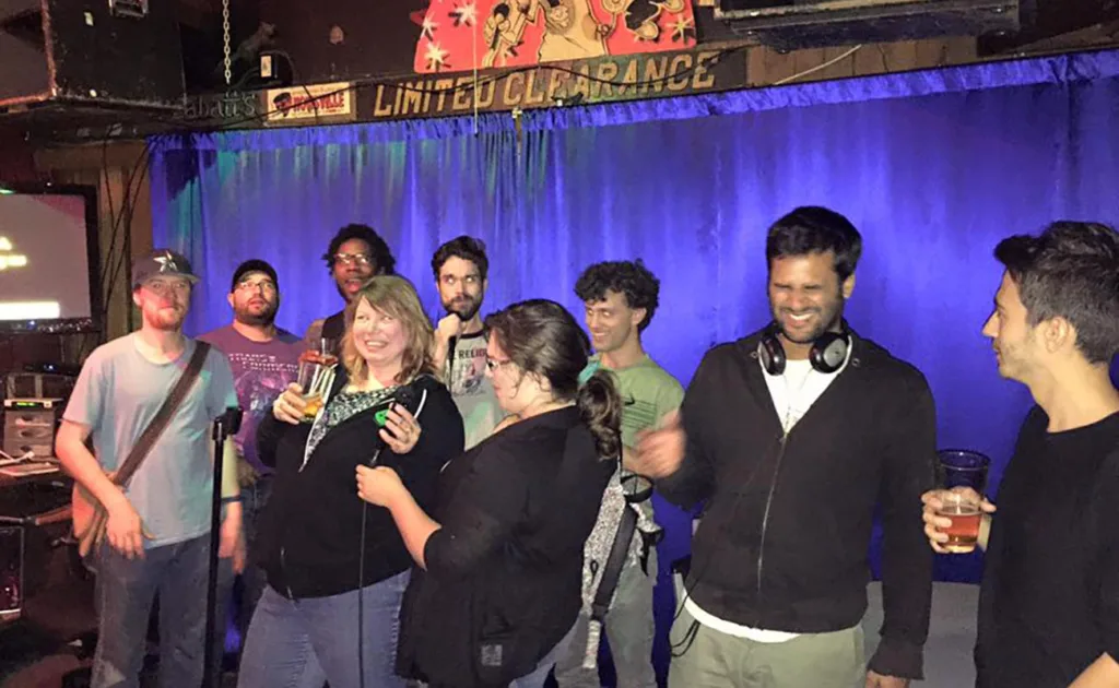 A group of people posing with drinks in hand in Monkey Pub on the karaoke stage