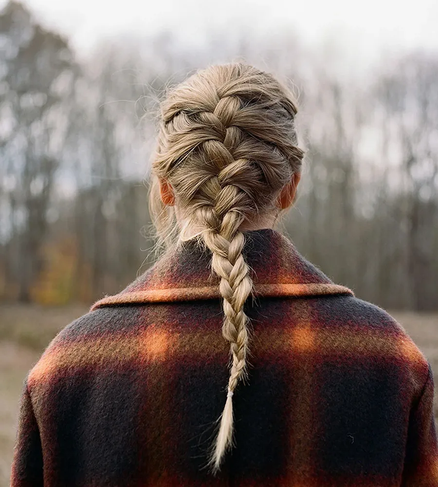 A cover image from Taylor Swift's new album that shows her from behind with a long braid. She looks out at a wintery wooden scene