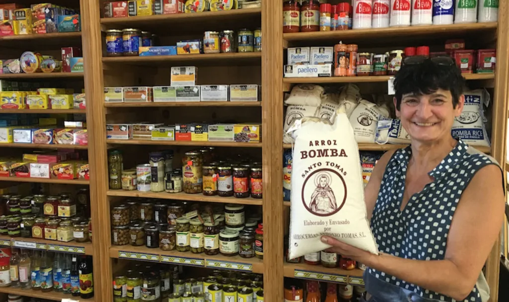 One of the owners of Paris-Madrid stands in front of a shelf of goods holding a bag of Bomba rice.
