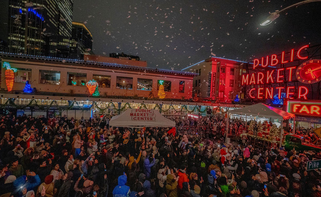 A huge crowd outside Pike Place Market during Christmastime while snow falls.