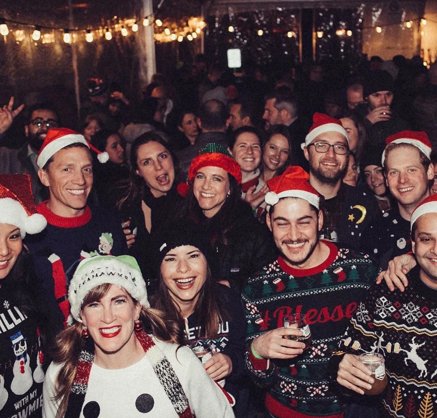 A group of people pose together in Christmas garb and Santa hats.