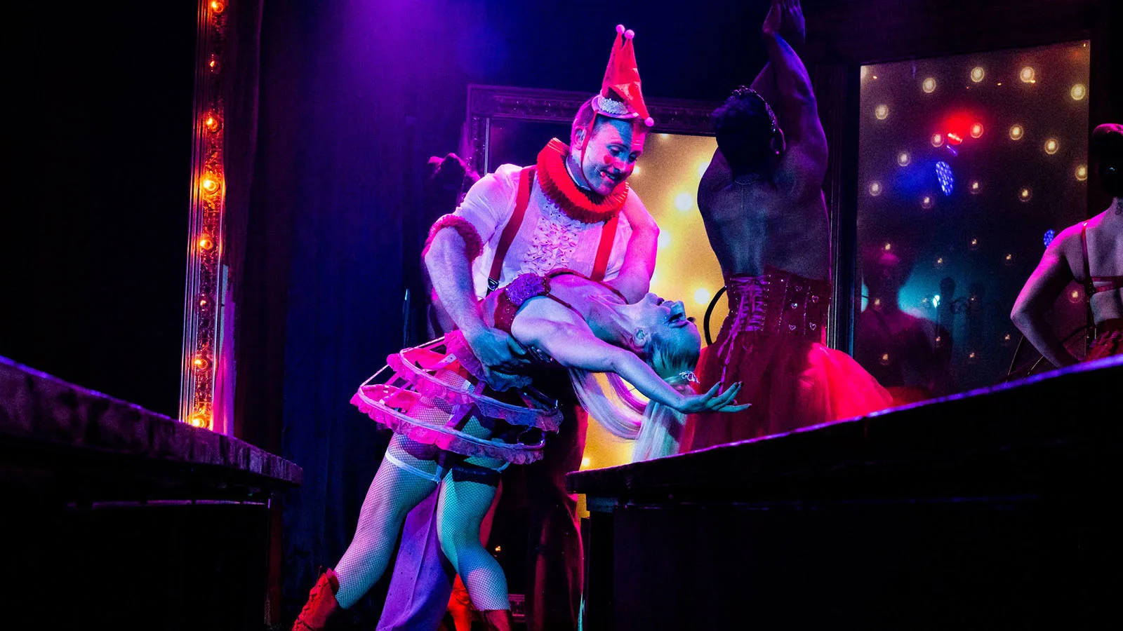 A man dips a women in a colorful and propped-filled stage.
