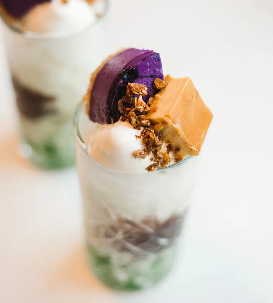 A bright and colorful filipino dessert served with ube cheesecake, halo halo, in a tall glass