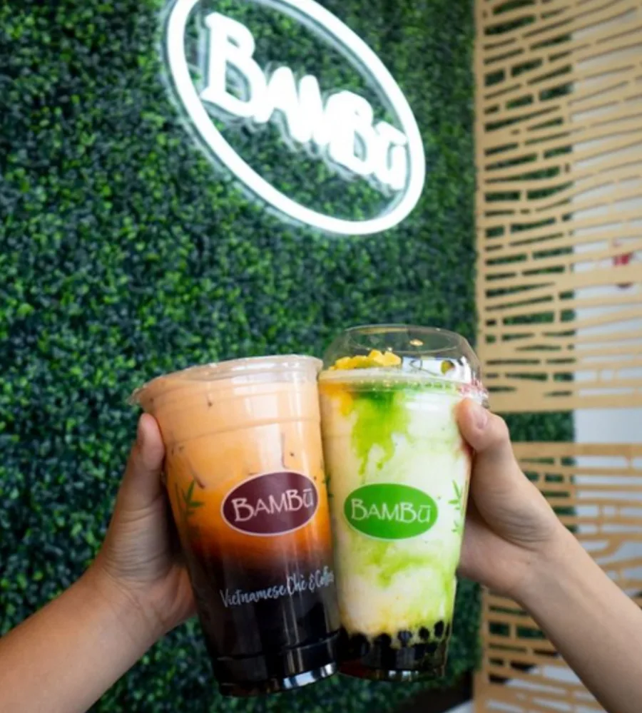 Two hands clink bright and colorful drinks together underneath a Bambu neon sign