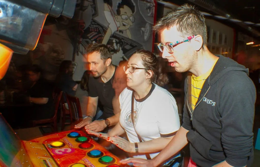 Three people stand side by side playing the Japanese arcade game, Bishi Bashi