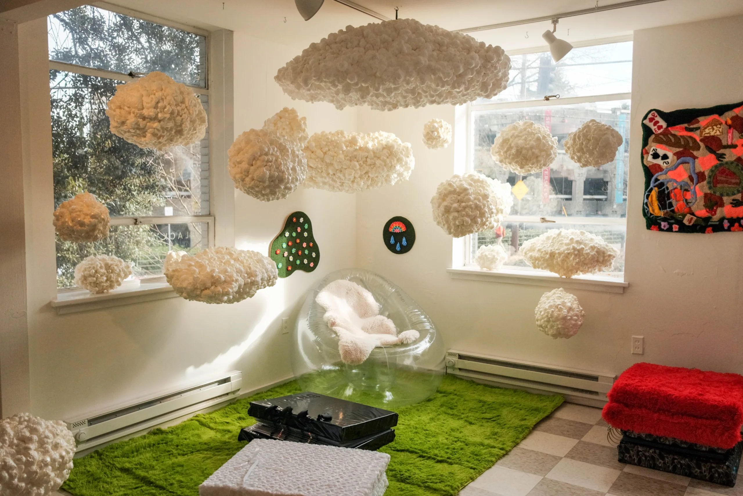 A corner room at Soft Touch in the Museum of Museums featuring an airy bean bag chair and light, white clouds made of fabric floating around it.