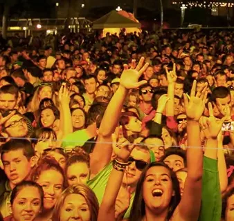 A crowd of people throw their hands up at the front of a stage at a night performance at a previous Bumbershoot