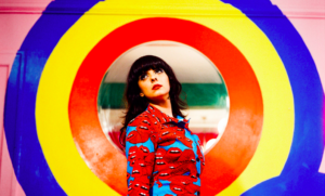 Spacemoth's Maryam Qudus stands in front of a bright ring of circles painted on a wall while looking into the air.