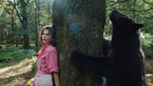 A woman leans against a tree, hiding, as the cocaine bear paws the other side