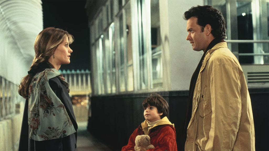 A screencap from Sleepless in Seattle. Annie Reed (Meg Ryan) and Sam Baldwin (Tom Hanks) stare at each other emotionally at a train station while Baldwin's son looks at Reed in the background.