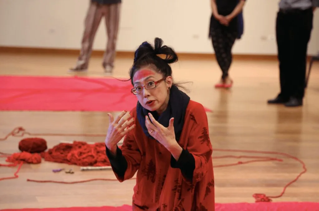 Artist Shoko Zama performs a workshop with a bunch of red fabric all around her