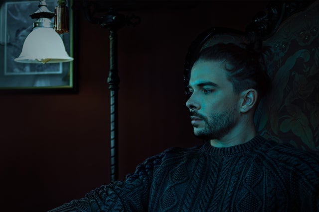 The performer Seven Lions looks toward a lamp with moody, blue-green lighting.