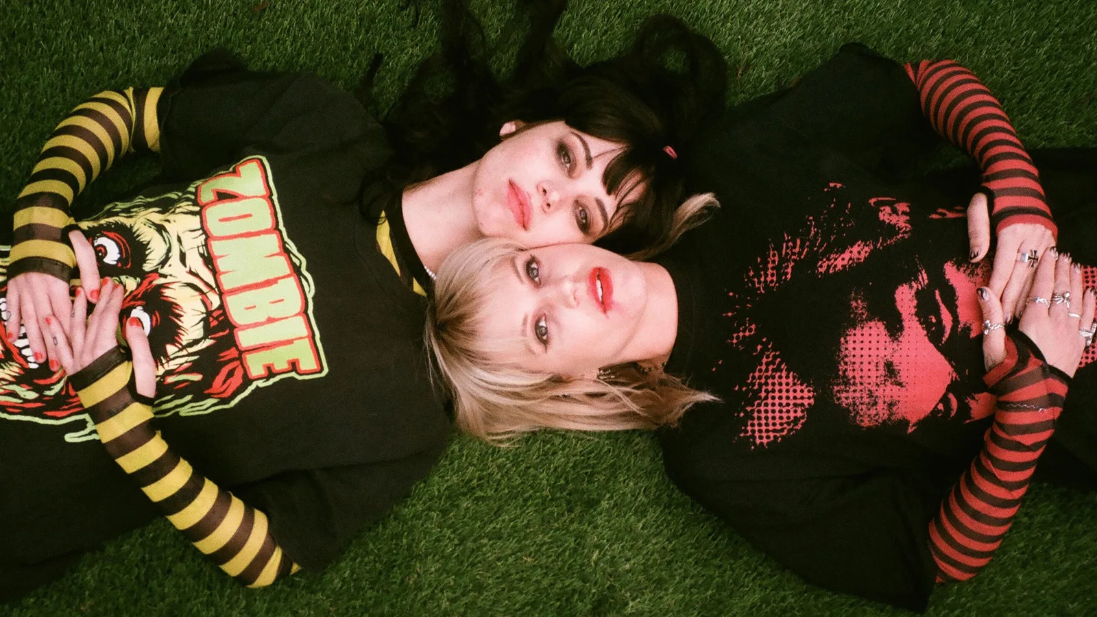 Mija and GG Magree of So Tuff So Cute lie on a grassy field, heads cradles against each other