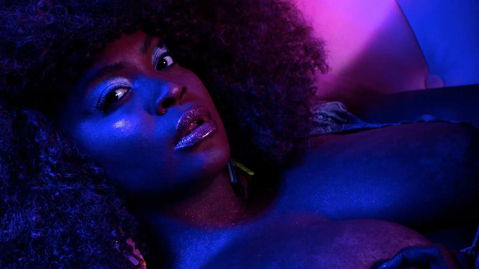 A closeup of burlesque performer Ms. Briq House in a reclined position. There's purple and indigo light illuminating her