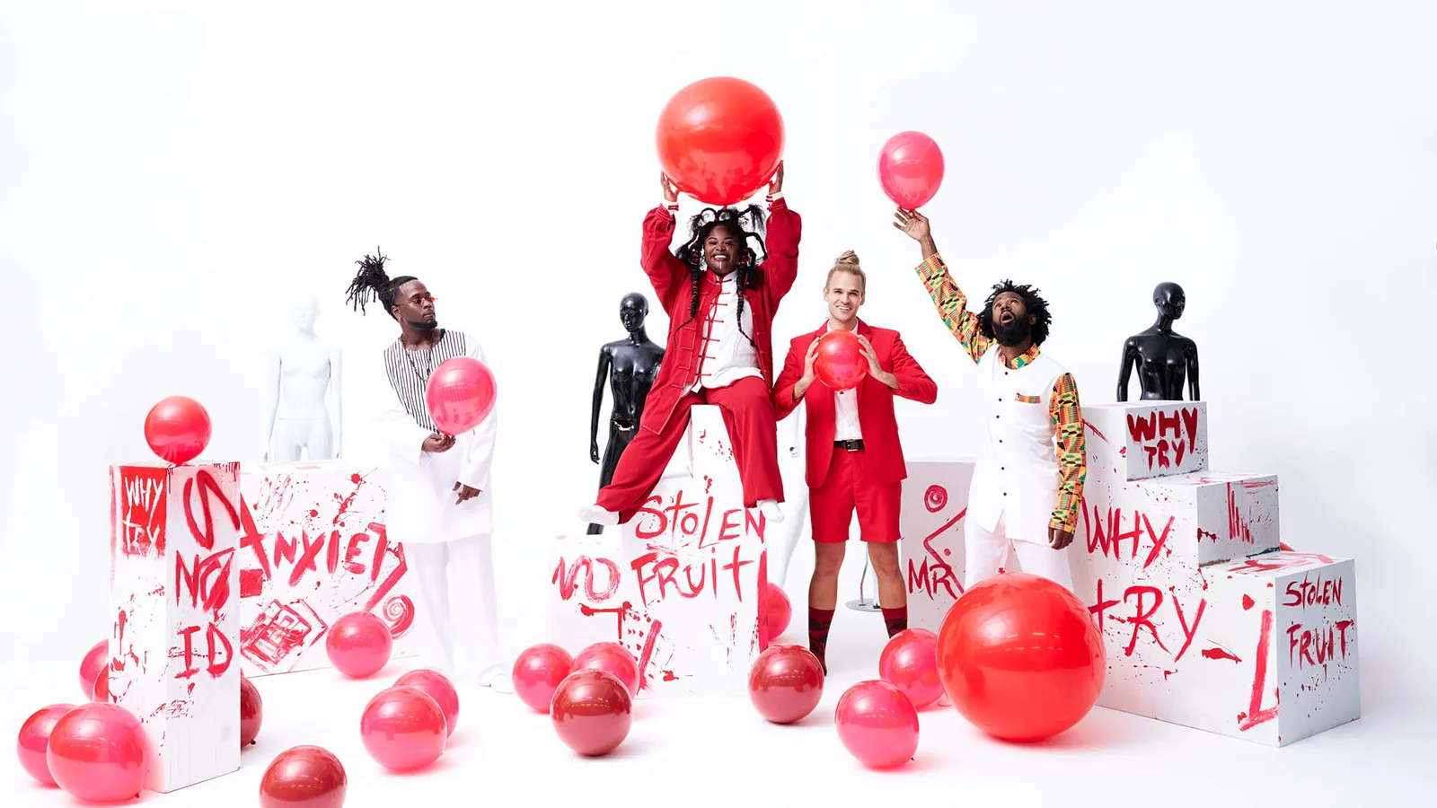 Music group Tank and the Bangas pose, smiling and laughing in a white room with big red balloons strewn everywhere.