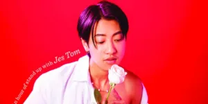 Jes Tom looks at a rose with a red background behind them