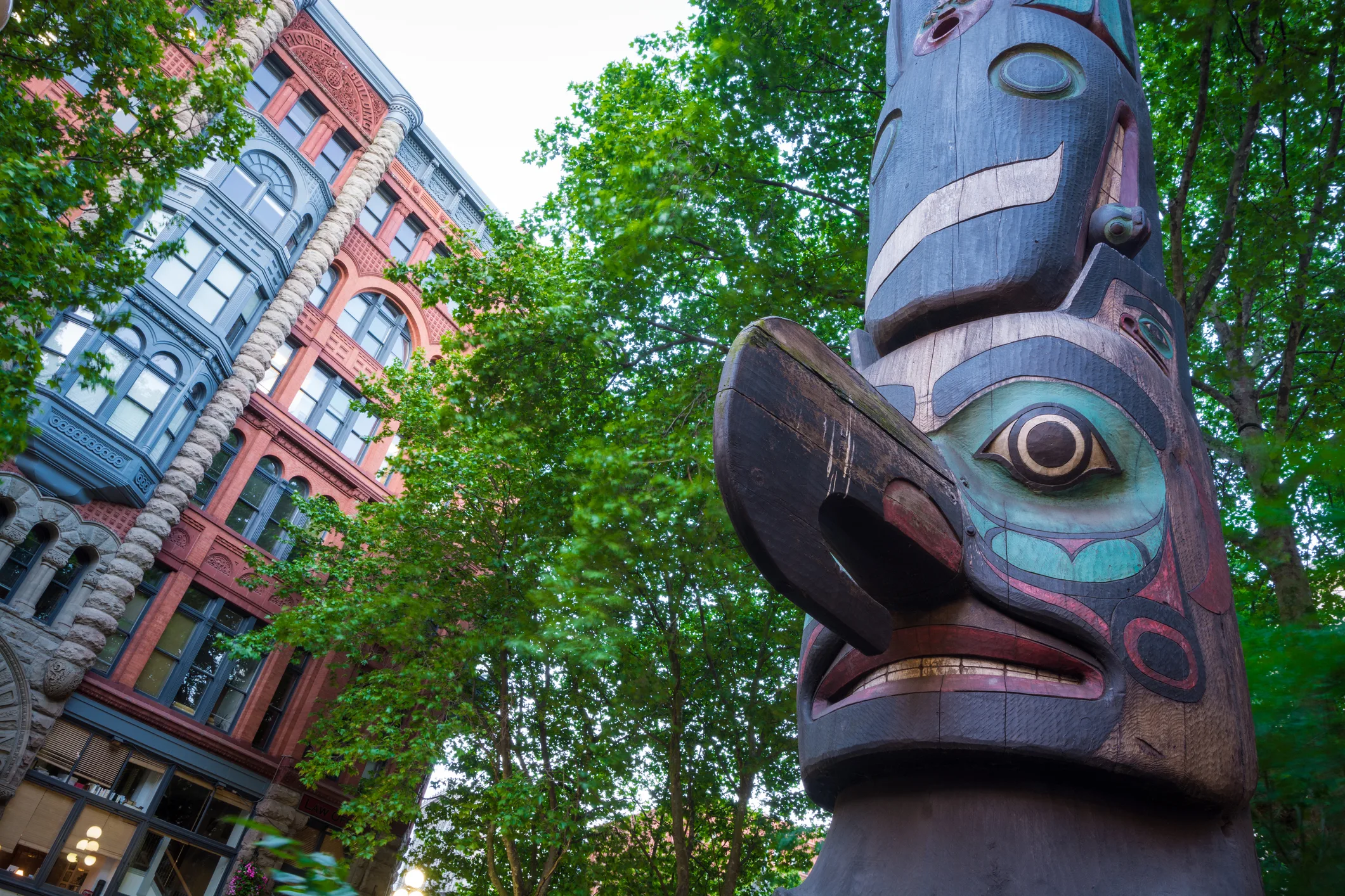 Totem pole at Pioneer Square in Seattle, WA with the Pioneer Building in the background, which was originally constructed in 1892.