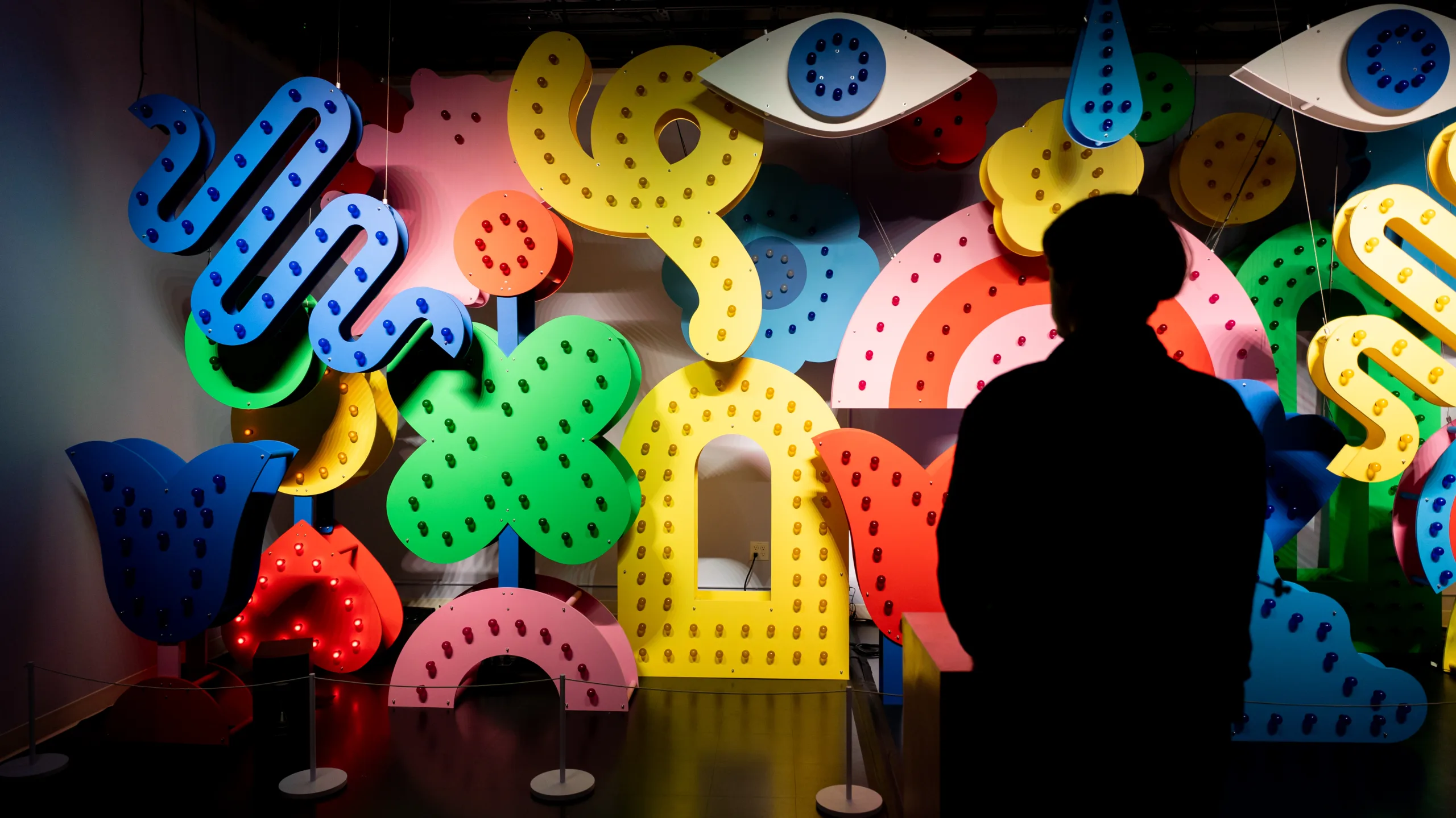 A person looks at a wall of light-up colorful shapes all in primary colors. It feels like a circus or Vegas.