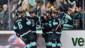 Seattle Kraken team members celebrate their win against Arizona Coyotes at Climate Pledge Arena. A crowd celebrates behind them.