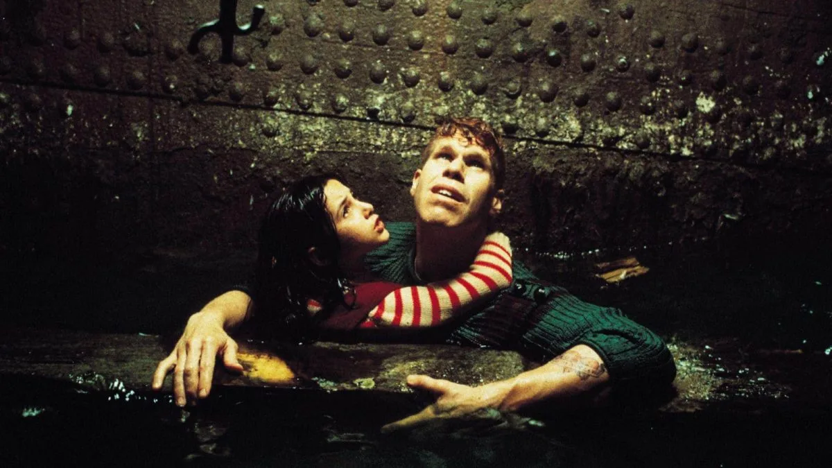 A screencap from "City of Lost Children." One holds Miette as they stay afloat in what looks to be a sewer.