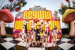A group of partiers stand in front of a giant Beyond Wonderland sign smiling. Some of them are dressed in rabbit costumes and others have instruments.