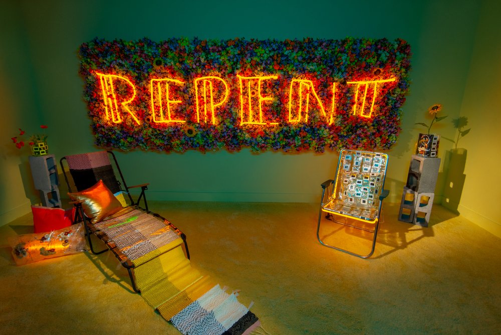 A colorful room with the words REPENT spelled in neon in the background. In the foreground, two chairs invite people to sit on them. Meryl Pataky (American, born 1983) with textile collaboration by Allie Felton. A Modern Guilt (installation view), 2020. Neon and mixed media; dimensions variable. Courtesy of artist. Photo by Deb Leal.