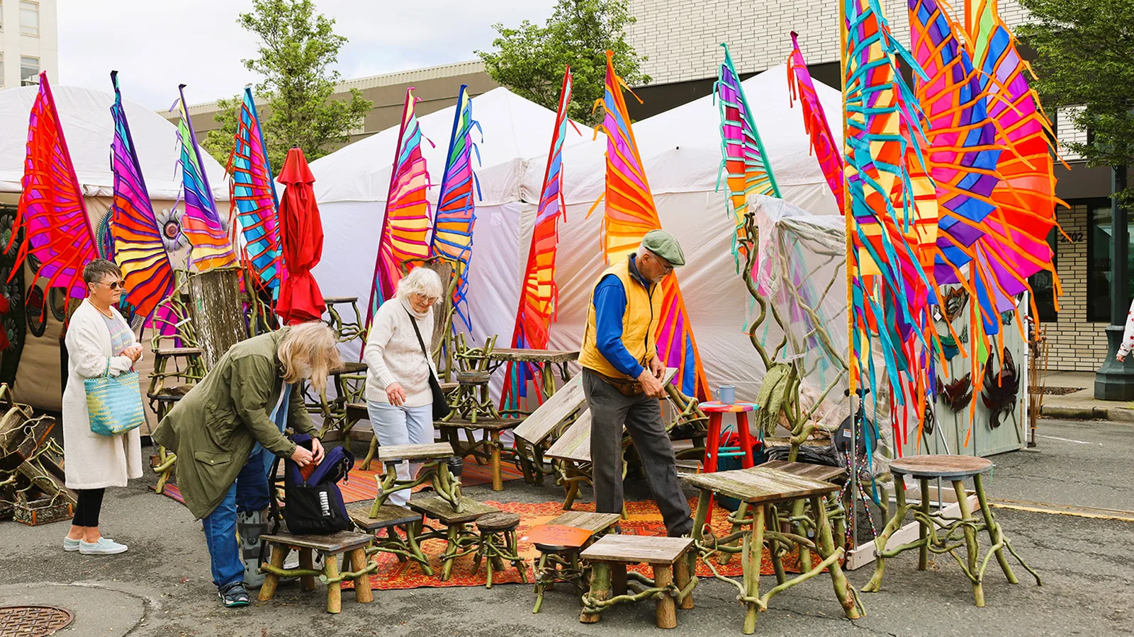 A group of people inspect outdoor furniture at Sorticulture. Tall colorful pole banners stand in the background