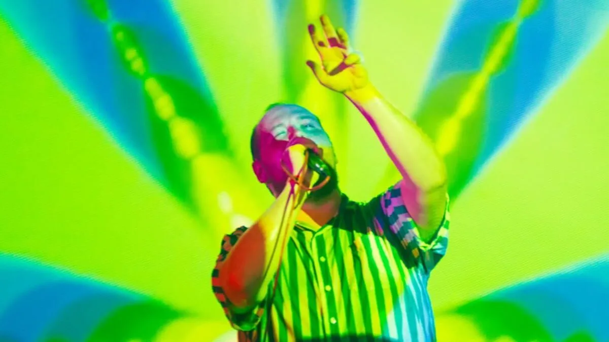 Dan Deacon sings onstage against a colorful, psychedelic background