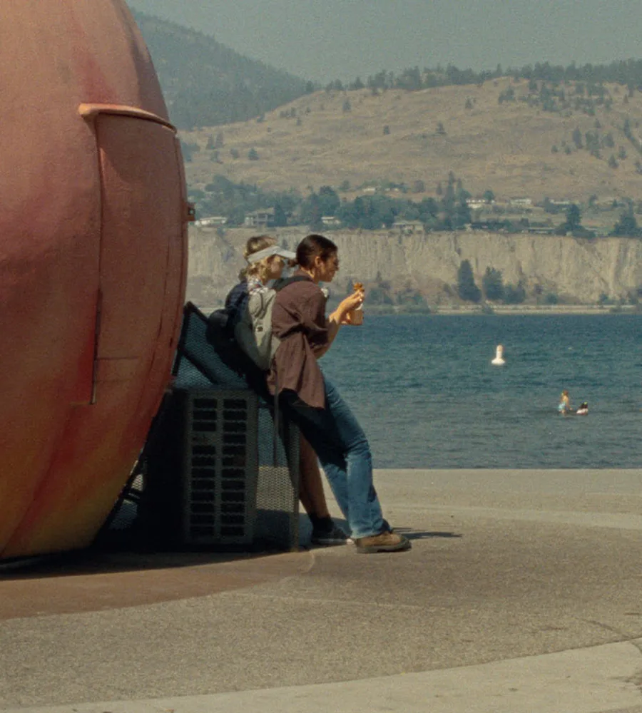 Two characters from the movie, Until Branches Bend lean against a giant peach statue and look out over the water.